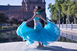 Middle-aged Hispanic woman in turquoise dress with rhinestones, twirling holding her dress while belly dancing. Belly dance concept.