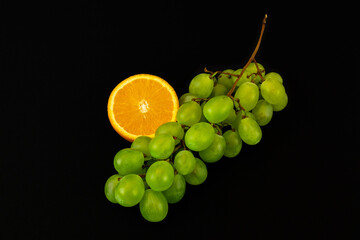 Sticker - Closeup shot of fresh slices of orange and green grapes isolated on a dark background