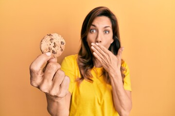 Sticker - Young latin woman holding cookie covering mouth with hand, shocked and afraid for mistake. surprised expression