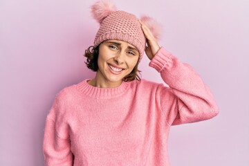 Wall Mural - Young brunette woman wearing cute wool cap confuse and wonder about question. uncertain with doubt, thinking with hand on head. pensive concept.