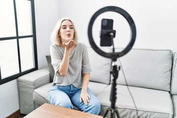 Poster - Young caucasian woman recording vlog tutorial with smartphone at home looking at the camera blowing a kiss with hand on air being lovely and sexy. love expression.