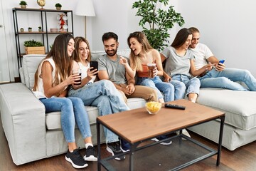 Group of young friends smiling happy and using smartphone sitting on the sofa at home.