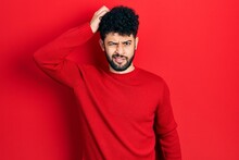 Young Arab Man With Beard Wearing Casual Red Sweater Confuse And Wonder About Question. Uncertain With Doubt, Thinking With Hand On Head. Pensive Concept.