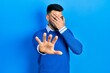 © Krakenimages.com - Young hispanic man with beard wearing casual blue sweater covering eyes with hands and doing stop gesture with sad and fear expression. embarrassed and negative concept.