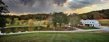 Aerial View Of Country Home Ranch With Pond And Trees At Sunset