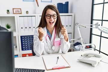 Poster - Young doctor woman wearing doctor uniform and stethoscope at the clinic excited for success with arms raised and eyes closed celebrating victory smiling. winner concept.