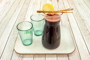 Pitcher of chicha morada with cinnamon stick, lemon wedge and two crystal glasses