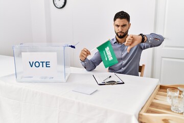 Poster - Young handsome man with beard at political campaign election holding arabia saudita flag with angry face, negative sign showing dislike with thumbs down, rejection concept