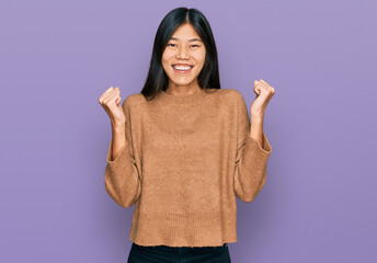 Sticker - Beautiful young asian woman wearing casual winter sweater celebrating surprised and amazed for success with arms raised and open eyes. winner concept.