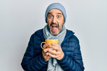 Poster - Middle age hispanic man wearing winter scarf and drinking a cup of hot coffee celebrating crazy and amazed for success with open eyes screaming excited.