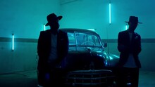 Two Silhouettes Of Men In Black Suits With Classic Hats Standing By Vintage Old Car. Strangers Look Like Italian Mafioso From Movie . Footage Have Permissible Count Of Normally Film Effect Style GRAIN