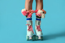 Legs Of Young Woman In Roller Skates With Flowers On Color Background
