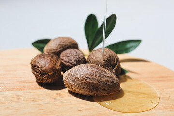 Pouring of essential oil onto board with shea nuts on light background, closeup