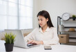© Chanakon - Young asian woman using laptop chatting video conference online sitting in living room at home. Business Woman looking at screen Meeting on social media live steam. Work, learning from home.