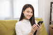 © Chanakon - Happy young asian woman looking at screen of smartphone sitting on sofa in living room she shopping online. She very happy. Teenage girl reading news from mobile phone feeling excited.