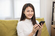 © Chanakon - Happy young asian woman looking at screen of smartphone sitting on sofa in living room she shopping online. She very happy. Teenage girl reading news from mobile phone feeling excited.