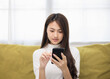 © Chanakon - Happy young asian woman looking at screen of smartphone sitting on sofa in living room she shopping online. She very happy. Teenage girl reading news from mobile phone feeling excited.