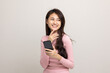 © Chanakon - Pretty young asian woman using smartphone standing on isolated white background feeling happy. Shopping online payment with mobile phone. Excited and surprised female holding cellphone.