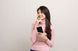 © Chanakon - Pretty young asian woman using smartphone standing on isolated white background feeling happy. Shopping online payment with mobile phone. Excited and surprised female holding cellphone.