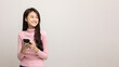 © Chanakon - Pretty young asian woman using smartphone standing on isolated white background feeling happy looking blank space. Shopping online payment with mobile phone. Excited female holding cellphone.