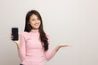 © Chanakon - Pretty young asian woman showing screen of smartphone and palm up hand holding something standing on isolated white background. She very happy.