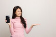 © Chanakon - Pretty young asian woman showing screen of smartphone and palm up hand holding something standing on isolated white background. She very happy.
