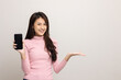 © Chanakon - Pretty young asian woman showing screen of smartphone and palm up hand holding something standing on isolated white background. She very happy.