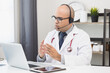 © Chanakon - Doctor talks to patient via online video conferencing with computer laptop wearing headset. Explain about taking medications to treat illnesses.