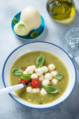 Plate of vegetable soup with addition of scamorza cheese and fresh green basil, vertical shot on a light-blue stone background