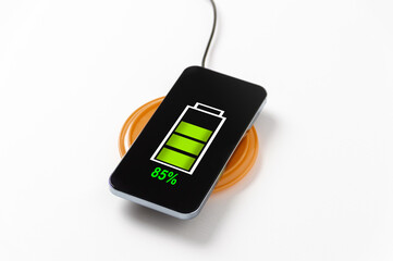 Close up of wireless charging of modern black glossy metal touchscreen smartphone on wireless power charger, with 85% charge sign in green