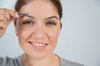 © Михаил Решетников - Close-up portrait of a caucasian woman doing eyebrow correction herself with tweezers