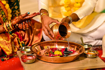 Wall Mural - Indian bride, groom pouring water into golden jar into tray with spices on marriage ceremony