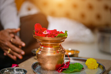 Wall Mural - Closeup shot of indian golden jar on tray with flowers, leaves and male hands background