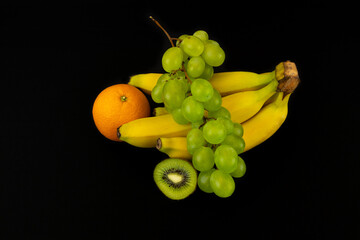 Wall Mural - Closeup shot of sliced kiwi, banana, grapes, and orange isolated on a dark background
