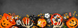 Halloween trick or treat bottom border with jack o lantern pails and mixed candy. Top view on a black banner background with copy space.