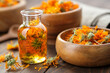 Bottle of calendula essential oil, infusion or serum, wooden bowl and mortar of dried healthy marigold flowers. Alternative medicine.