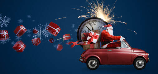 Wall Mural - Christmas is coming. Santa Claus on toy car delivering New Year 2022 gifts and countdown clock at blue background with fireworks