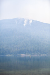 Wildfires burn on a forested mountain on July 16th, 2021, at Three Valley Gap lake, between Revelstoke and Sicamous, British-Columbia. The lake is cloaked in smoke from the fires raging in the area.