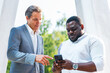 © Acronym - African-American businessman and his colleague in front of modern office building. Financial investors are talking outdoor. Banking and business concept.
