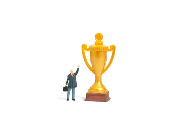 Miniature people toy figure photography. A businessman standing in front of gold trophy determine to win or become a winner while raise his hand. Isolated on white background