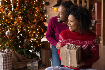 Wall Mural - Smiling African American couple celebrate Christmas at home look in distance dream of happy future together. Smiling biracial man and woman enjoy New Year winter holidays make wish visualize.