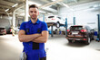 © My Ocean studio - Confident handsome young and experienced car repair worker in work overalls posing against the background of lifted cars in a car service