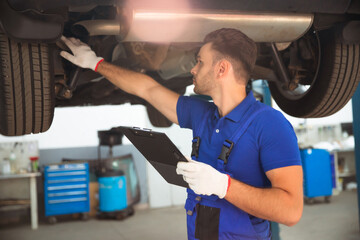 Wall Mural - Confident and concentrated young and experienced car repair specialist with a tablet in his hand inspects and diagnosis the car for breakdowns