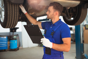 Wall Mural - Confident and concentrated young and experienced car repair specialist with a tablet in his hand inspects and diagnosis the car for breakdowns