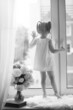 © alexkich - A little girl is sitting on the windowsill. A bouquet of flowers in a vase by the window and a girl sniffing flowers. A little princess in a white dress with a bouquet of white flowers by window.
