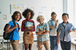 © insta_photos - Portrait of cheerful smiling diverse schoolchildren standing posing in classroom holding notebooks and backpacks looking at camera happy after school reopen. Diversity. Back to school concept.