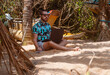 Cyfrowy nomada, mężczyzna pracujący z laptopem oraz smartfonem na plaży w tropikalnym otoczeniu.