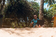 Cyfrowy nomada, mężczyzna pracujący z laptopem oraz smartfonem na plaży w tropikalnym otoczeniu.