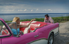 Young Man Pushing Pink Vintage Convertible At Coast Whilst Girlfriend Drives, Havana, Cuba