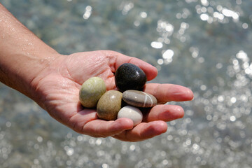 Smooth pebbles of different colors in the palm.Sea ​​background